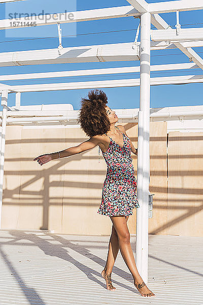 Junge Frau im Sommerkleid  die auf einer Terrasse das Sonnenlicht genießt
