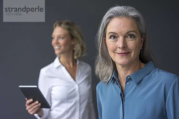 Porträt einer selbstbewussten reifen Geschäftsfrau mit einer jungen Geschäftsfrau im Hintergrund