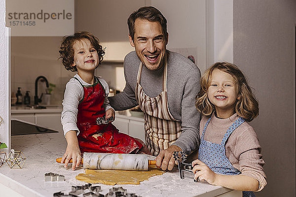 Glücklicher Vater mit zwei Töchtern  die in der Küche Weihnachtsplätzchen backen