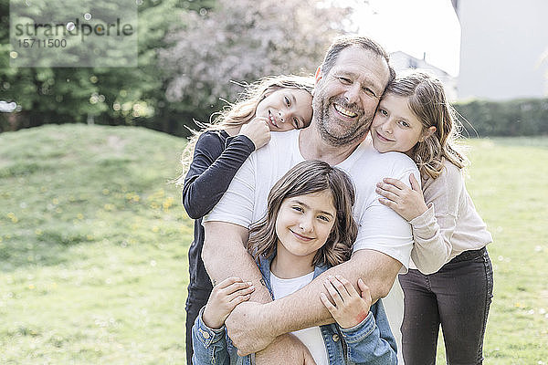 Porträt eines glücklichen Vaters mit drei Drillings-Töchtern auf einer Wiese