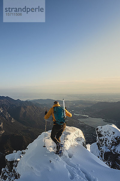 Bergsteiger erreicht den Gipfel eines verschneiten Berges und genießt die Aussicht  Lecco  Italien