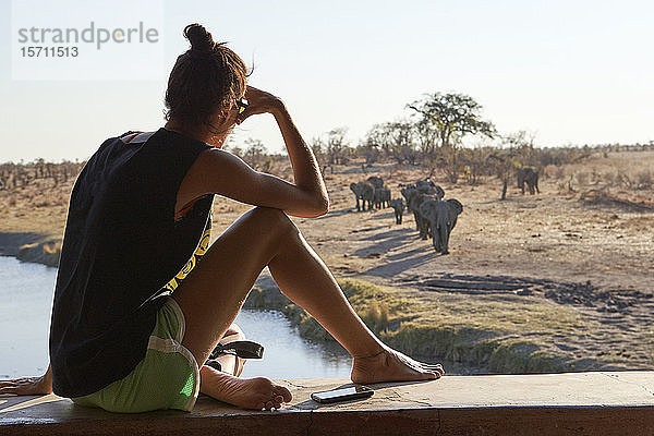 Frau beobachtet eine Elefantenherde im Fluss von einem Aussichtspunkt aus  Hwange-Nationalpark  Simbabwe