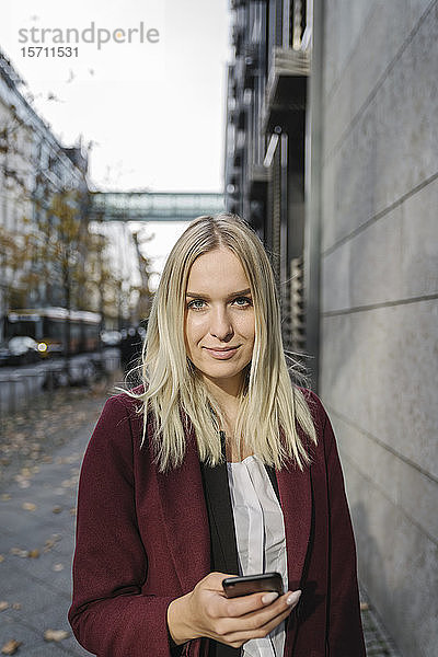 Blonde Geschäftsfrau mit Smartphone im Hintergrund moderne Gebäude