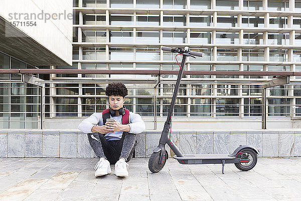 Junger Mann mit E-Scooter entspannt und benutzt Smartphone