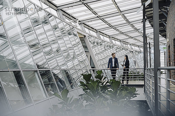 Geschäftsmann und Geschäftsfrau stehen auf einem Skywalk in einem modernen Bürogebäude