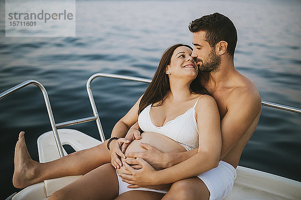 Romantisches Paar mit schwangerer Frau auf Boot sitzend