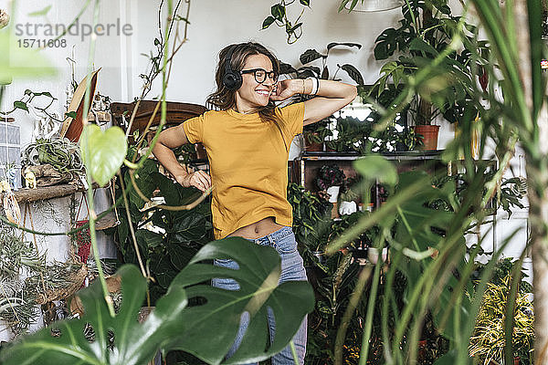 Fröhliche junge Frau  umgeben von Pflanzen  die mit Kopfhörern Musik hört