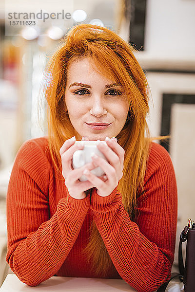 Porträt einer lächelnden jungen Frau mit orange gefärbten Haaren  die eine Tasse Kaffee trinkt