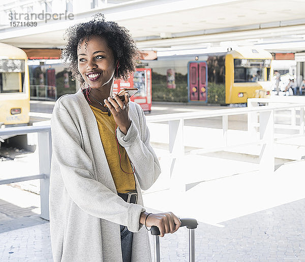 Glückliche junge Frau mit Kopfhörern  die ein Smartphone am Bahnsteig benutzt
