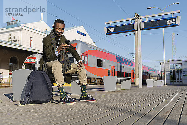Eleganter Mann benutzt Smartphone beim Warten auf den Zug