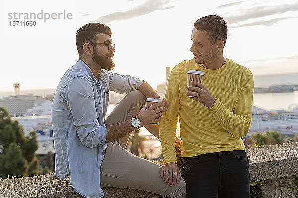 Schwules Paar mit Kaffee zum Mitnehmen auf einem Aussichtspunkt über der Stadt mit Blick auf den Hafen  Barcelona  Spanien