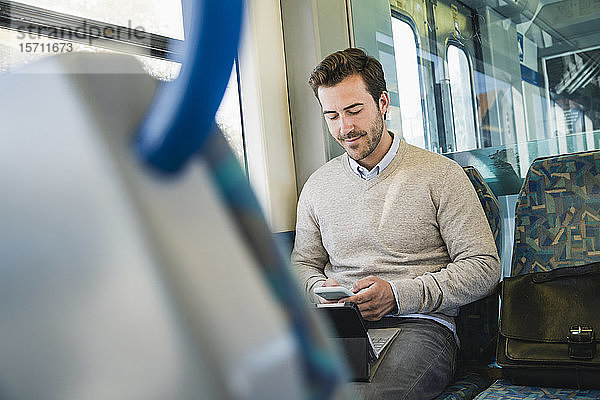 Junger Mann benutzt Smartphone und Tablet in einem Zug