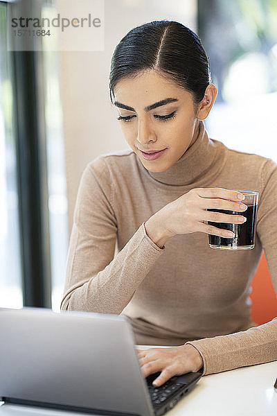 Junge Frau bei einem Drink und mit Laptop in einem Café