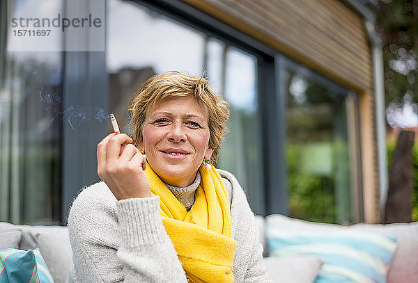 Porträt einer Frau  die zu Hause auf der Terrasse eine Zigarette raucht