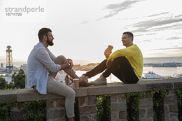 Zwei Männer sitzen auf einer Mauer auf einem Aussichtspunkt über der Stadt mit Blick auf den Hafen  Barcelona  Spanien