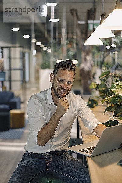 Portrait eines lächelnden reifen Geschäftsmannes mit Laptop in moderner Büro-Lounge