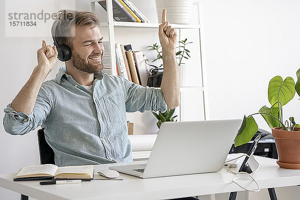 Aufgeregter Mann hört Musik am Schreibtisch im Büro
