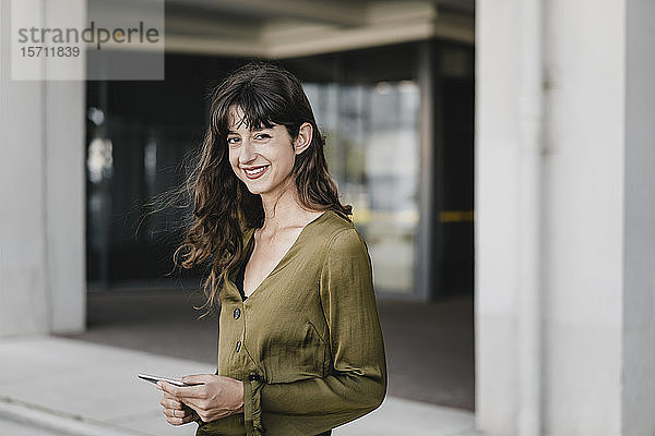 Porträt einer lächelnden brünetten Frau mit Smartphone in der Hand