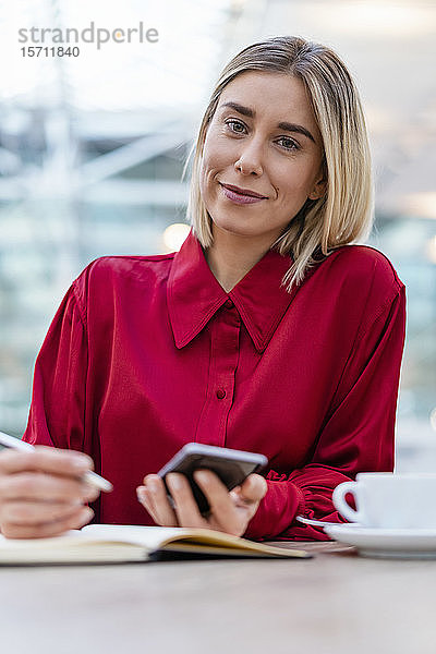 Porträt einer jungen Geschäftsfrau mit Handy  die sich in einem Cafe Notizen macht