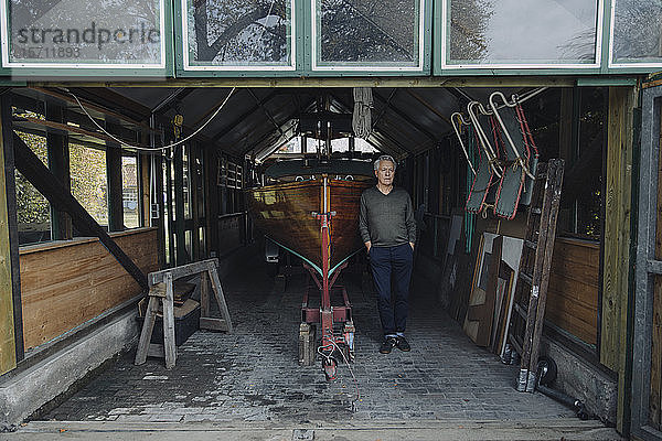 Älterer Mann steht an einem Holzboot in einem Bootshaus