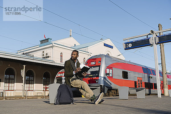 Stilvoller Mann mit Dokumenten  der auf den Zug wartet