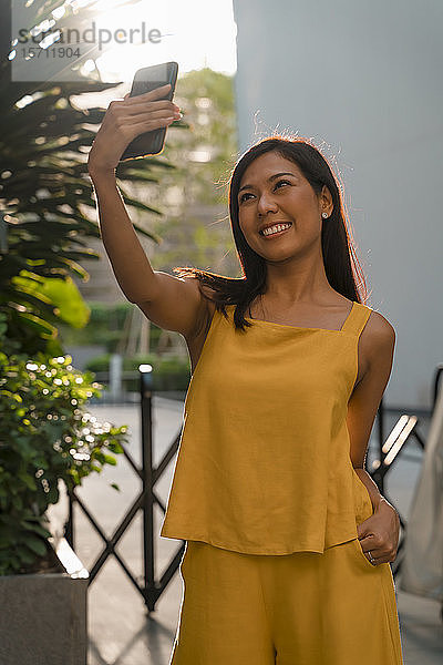 Porträt einer modischen  gelb gekleideten Frau  die sich mit einem Smartphone selbstständig macht