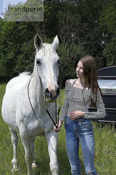 Glückliche Teenagerin mit Pferd auf der Wiese stehend