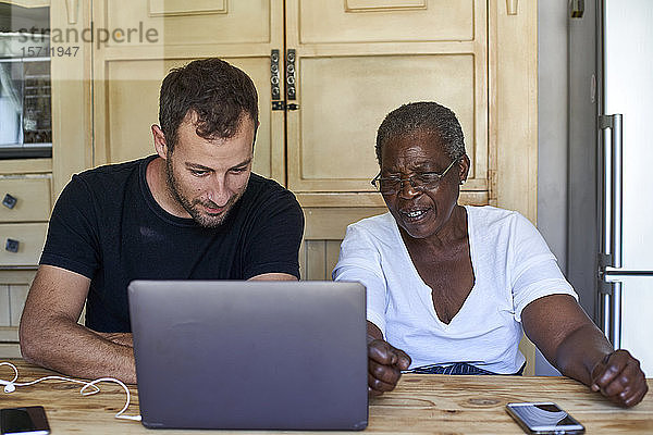 Ältere Frau und Mann sitzen am Küchentisch und teilen sich einen Laptop