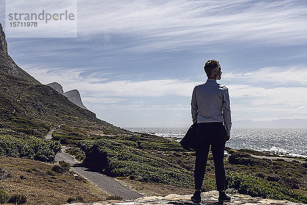 Rückenansicht eines Geschäftsmannes  der auf einem Plateau steht und auf das Meer schaut  Cape Point  Westkap  Südafrika