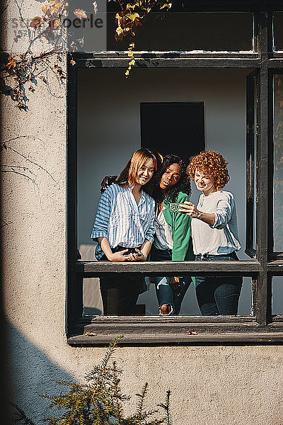 Drei Geschäftsfrauen  die am Fenster eines Bürogebäudes stehen und sich ein Selfie