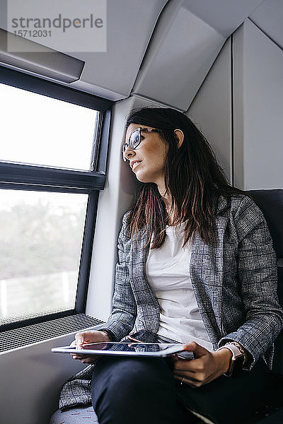 Brünette Frau auf der Fahrt mit dem Zug zur Arbeit  mit einer Tablette in der Hand