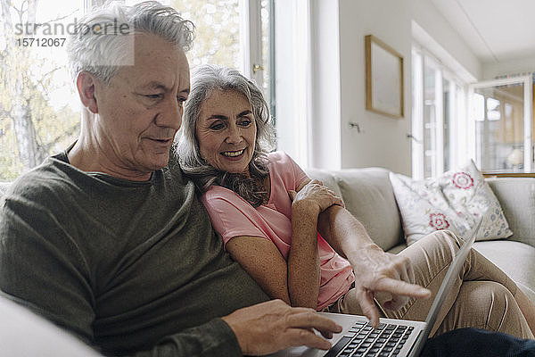 Glückliches älteres Ehepaar mit Laptop zu Hause auf der Couch