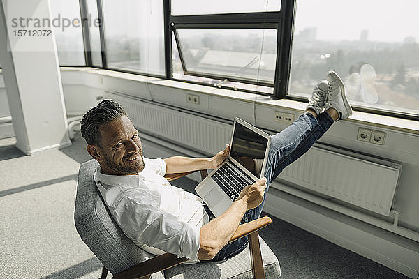 Porträt eines lächelnden reifen Geschäftsmannes mit Laptop in einem leeren Büro
