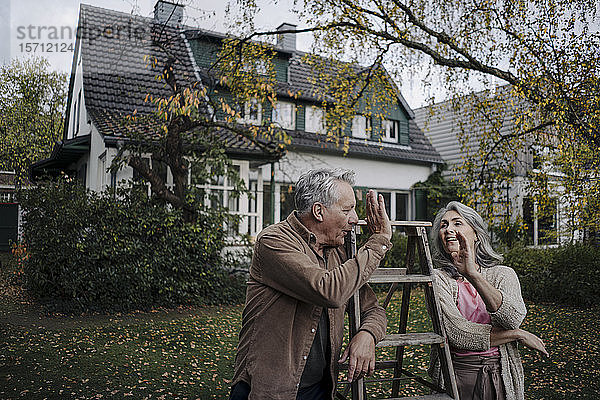 Älteres Ehepaar mit einer Leiter im Garten seines Hauses