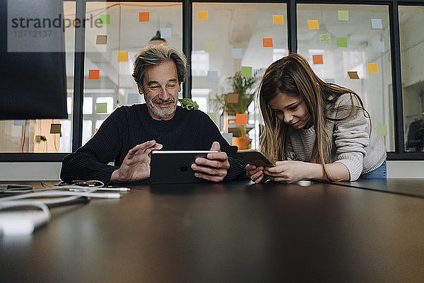 Gelegenheitskaufmann und -mädchen mit Tablet und Smartphone im Büro