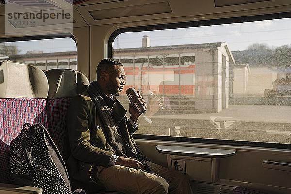 Stilvoller Mann trinkt im Zug Heißgetränk aus wiederverwendbaren Bechern