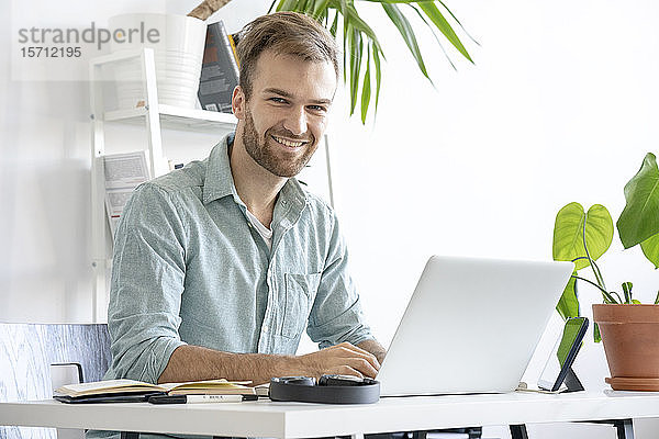 Porträt eines lächelnden Mannes mit Laptop am Schreibtisch im Büro