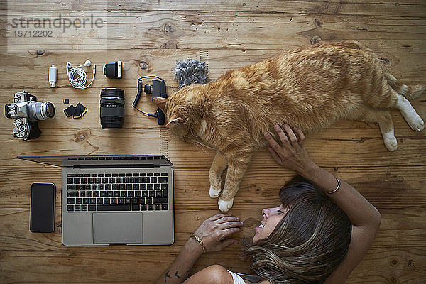 Erschöpfte Frau schläft auf dem Tisch mit Ingwer-Katze  Laptop und Fotoausrüstung