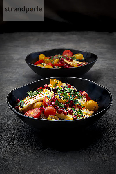 Schalen mit persischem Salat mit Tomaten  gegrilltem Halloumi-Käse  Auberginen  Granatapfelkernen  Sumach  schwarzem Sesam und Petersilie