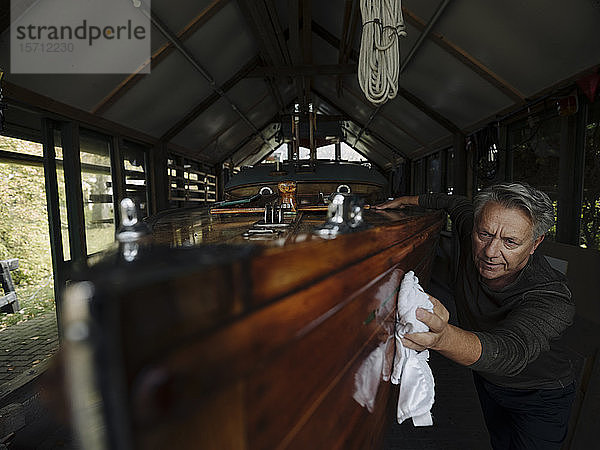 Älterer Mann reinigt Holzboot in einem Bootshaus