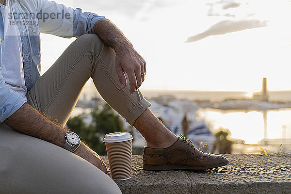 Nahaufnahme eines auf einer Mauer sitzenden Mannes auf einem Aussichtspunkt über der Stadt mit Blick auf den Hafen  Barcelona  Spanien