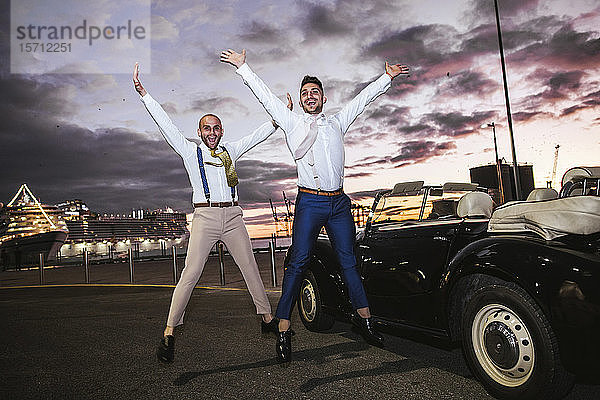 Elegantes schwules Paar springt bei Sonnenuntergang auf ein Oldtimer-Cabriolet