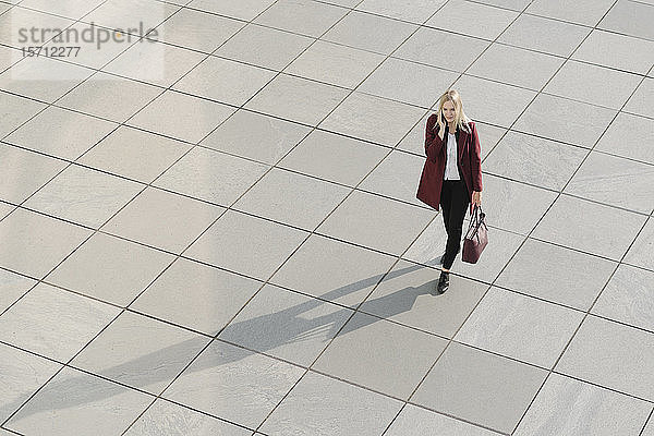 Blick von oben auf eine blonde Geschäftsfrau mit Smartphone  die auf Betonboden geht