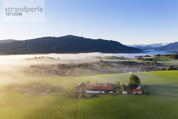 Deutschland  Oberbayern  Greiling  Luftaufnahme von Dorf und Feldern im Nebel bei Sonnenaufgang