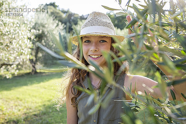 Lächelndes Mädchen mit Strohhut steht in einem Olivenhain  Toskana  Italien