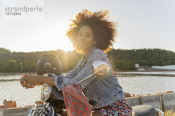 Junge Frau sitzt bei Sonnenuntergang auf einem Motorroller  Ibiza