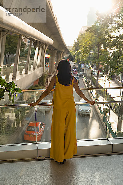 Rückenansicht einer modischen  gelb gekleideten Frau  die auf einer Brücke steht  Bangkok  Thailand