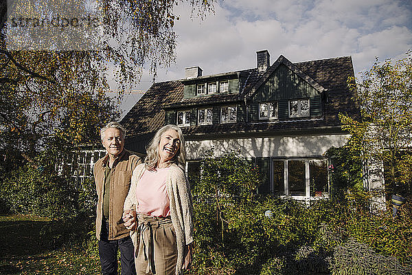 Glückliches älteres Ehepaar im Herbst im Garten ihres Hauses