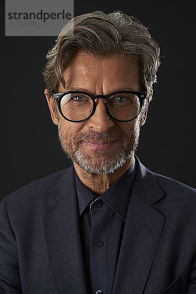 Porträt eines lächelnden reifen Geschäftsmannes mit Brille vor dunklem Hintergrund