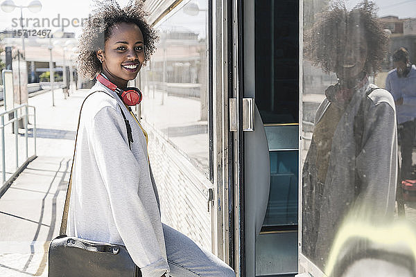 Porträt einer lächelnden jungen Frau beim Einsteigen in einen Zug